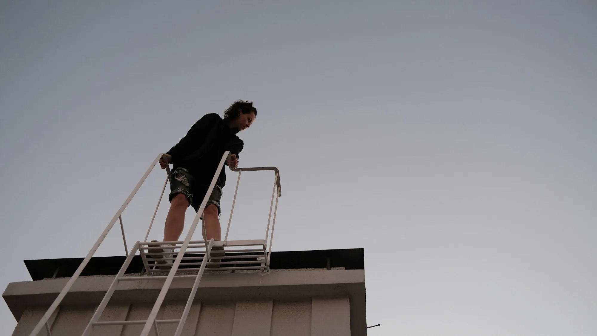Man stepping off a roof-access ladder onto a flat roof