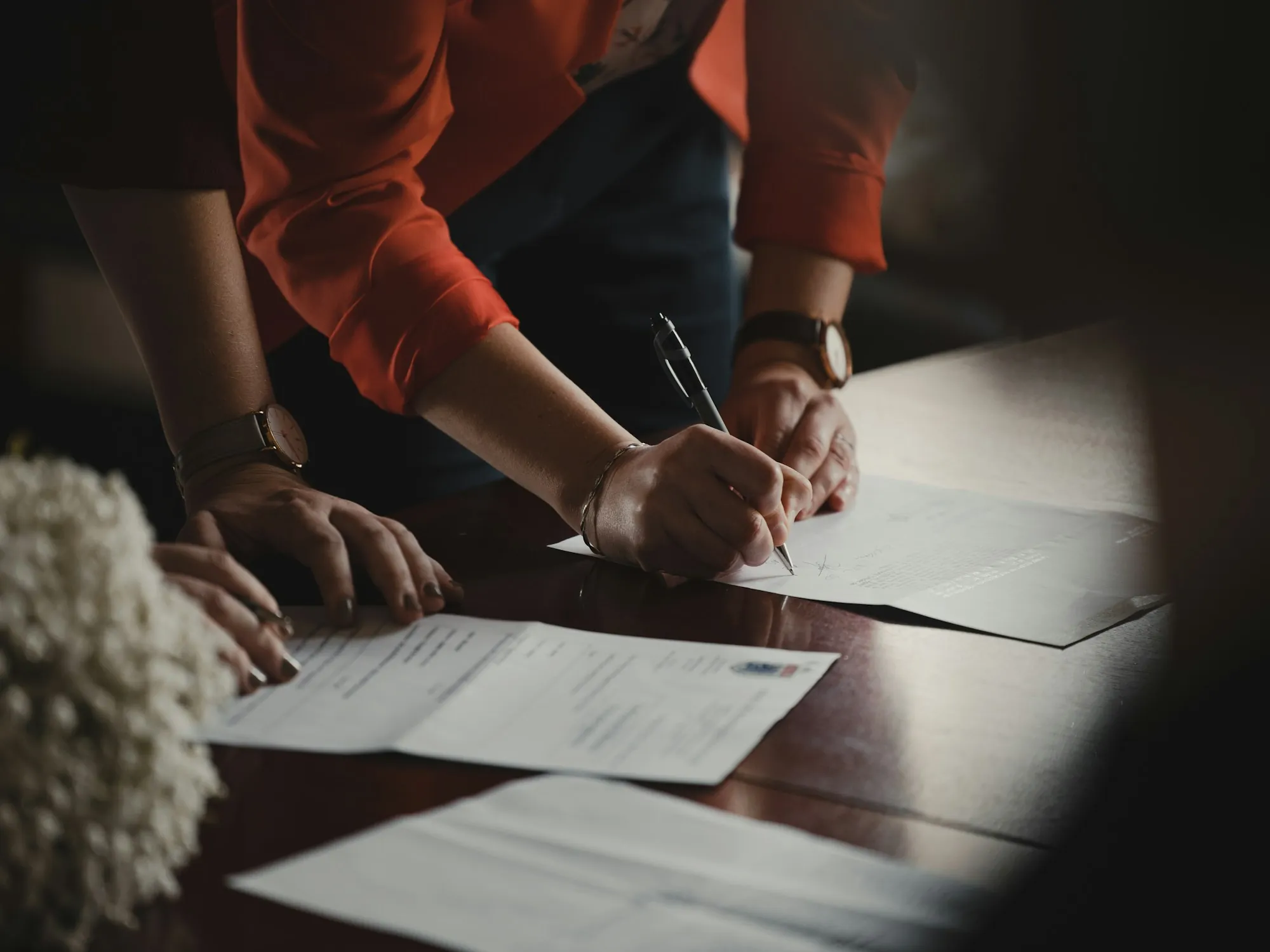 Hands signing documents on a wooden table