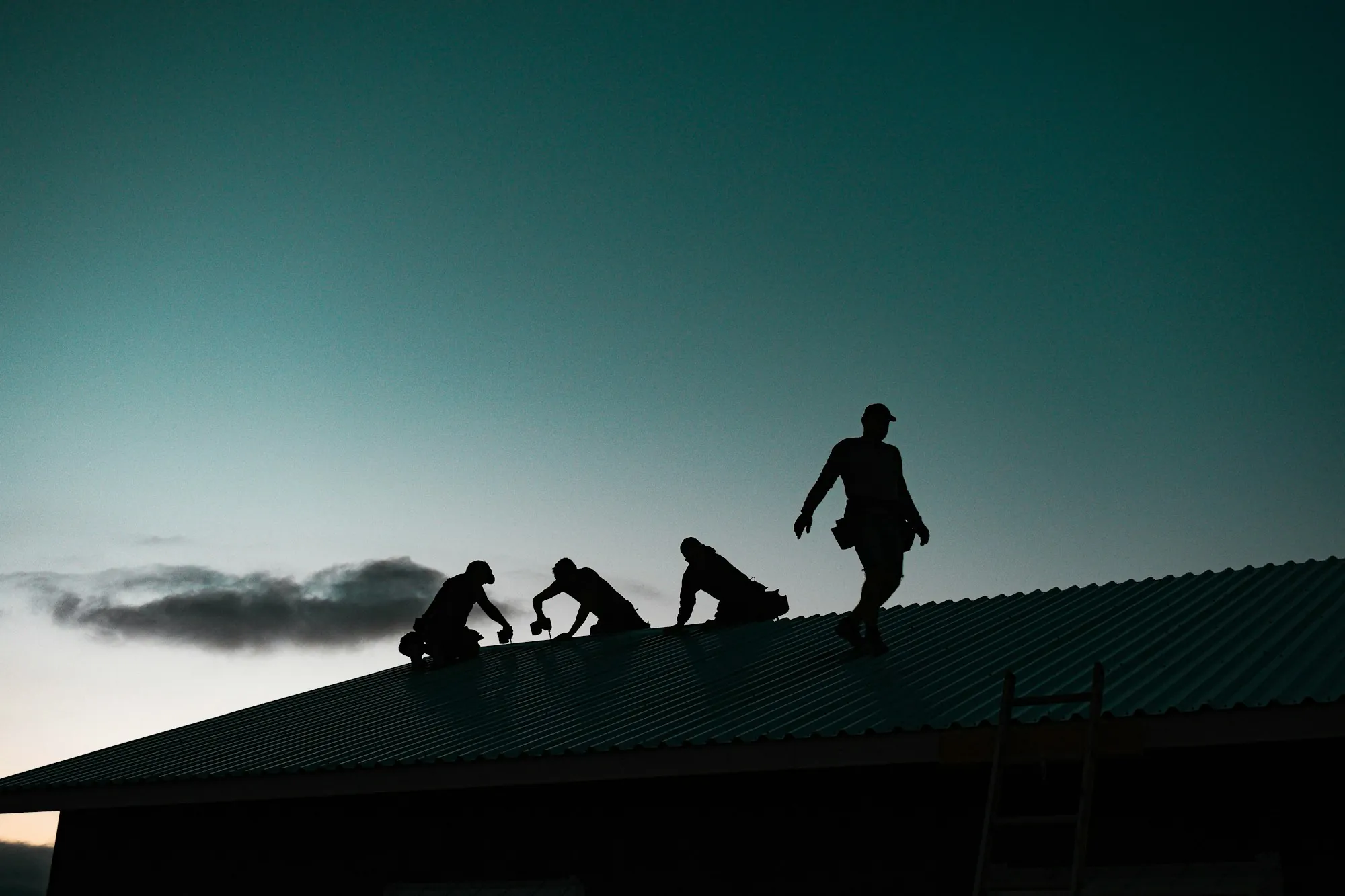 Silhouettes of a roofing crew working on a roof at dusk