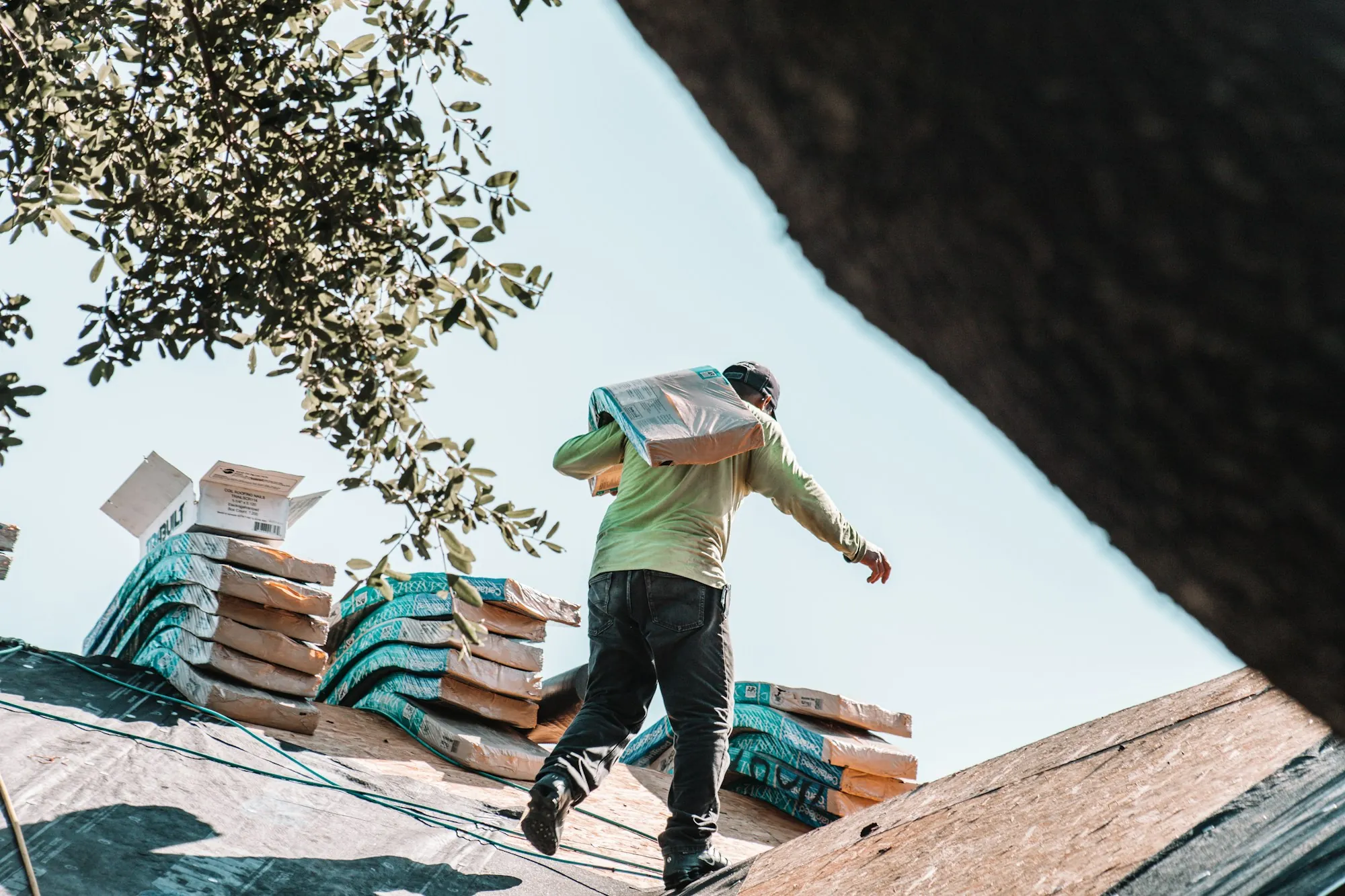 Roofer carrying a bundle of shingles across a sloped roof